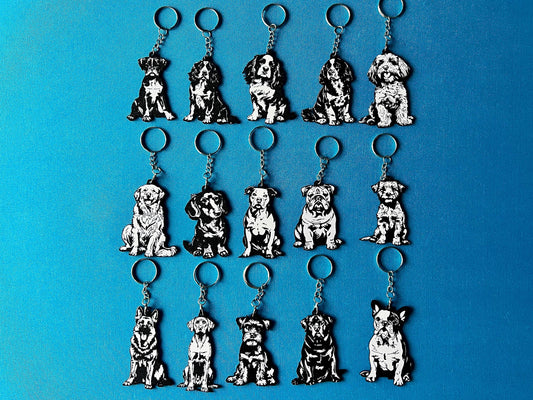 15 Dog breed Silhouette Keyrings laying on a blue table cloth. The keyrings feature a white background with a black silhouette of a dog.