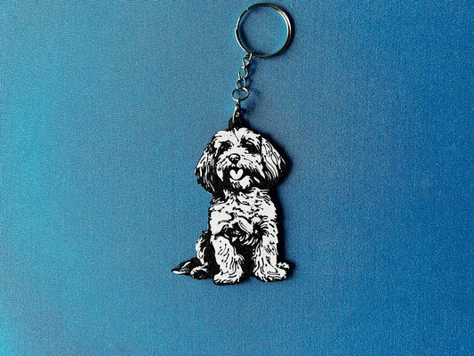 Cockapoo Silhouette Keyring laying on a blue table cloth. The keyring features a white background with a black silhouette of a Cockerpoo.