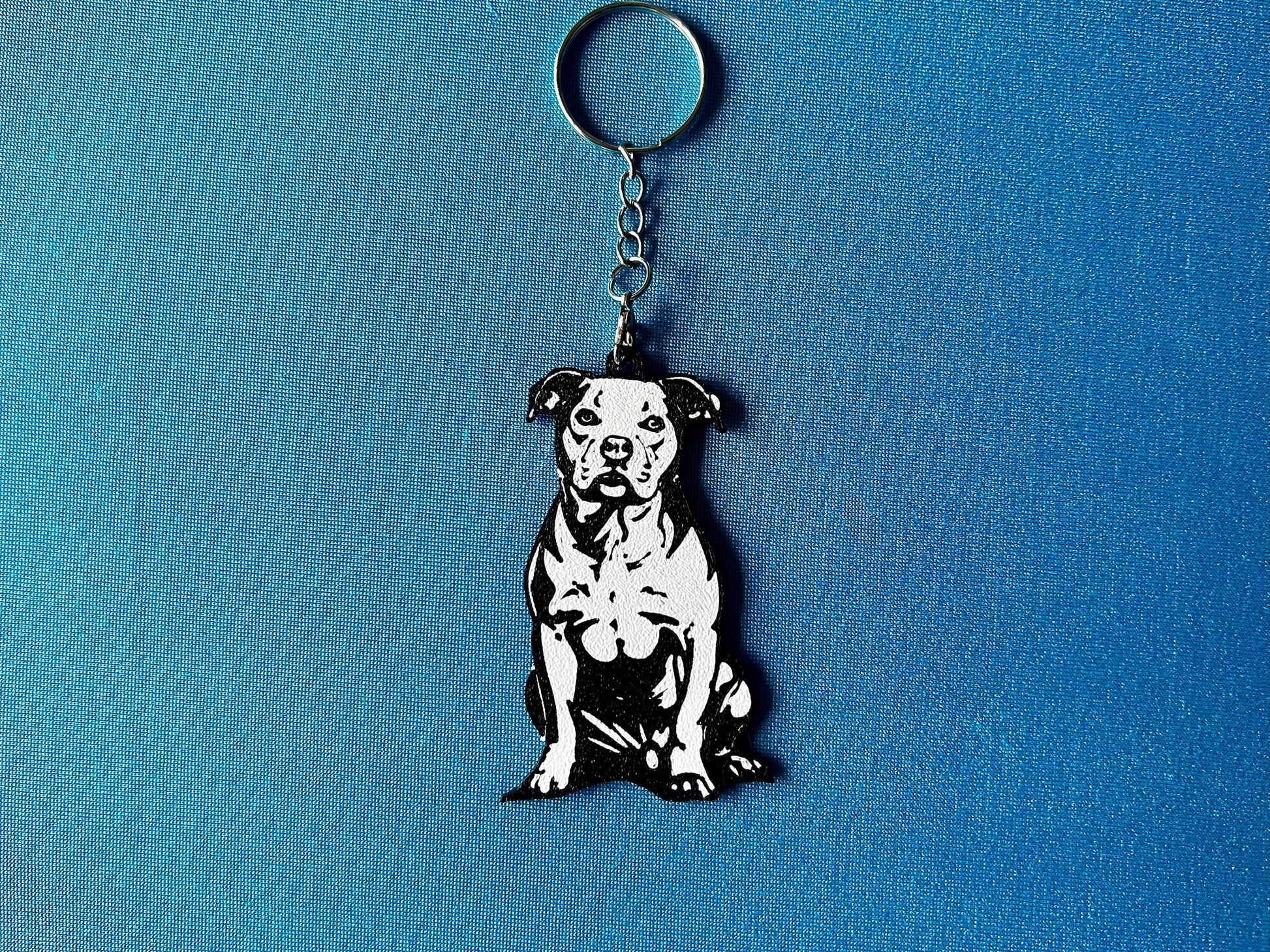 Staffordshire Bull Terrier Silhouette Keyring laying on a blue table cloth. The keyring features a white background with a black silhouette of a Staffordshire Bull Terrier.