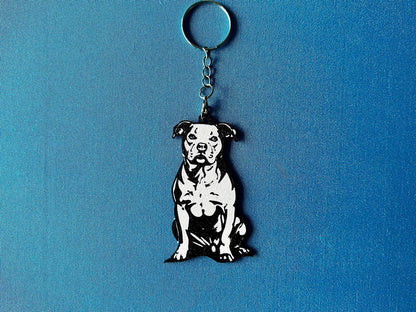 Staffordshire Bull Terrier Silhouette Keyring laying on a blue table cloth. The keyring features a white background with a black silhouette of a Staffordshire Bull Terrier.