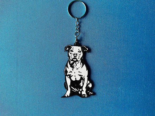 Staffordshire Bull Terrier Silhouette Keyring laying on a blue table cloth. The keyring features a white background with a black silhouette of a Staffordshire Bull Terrier.