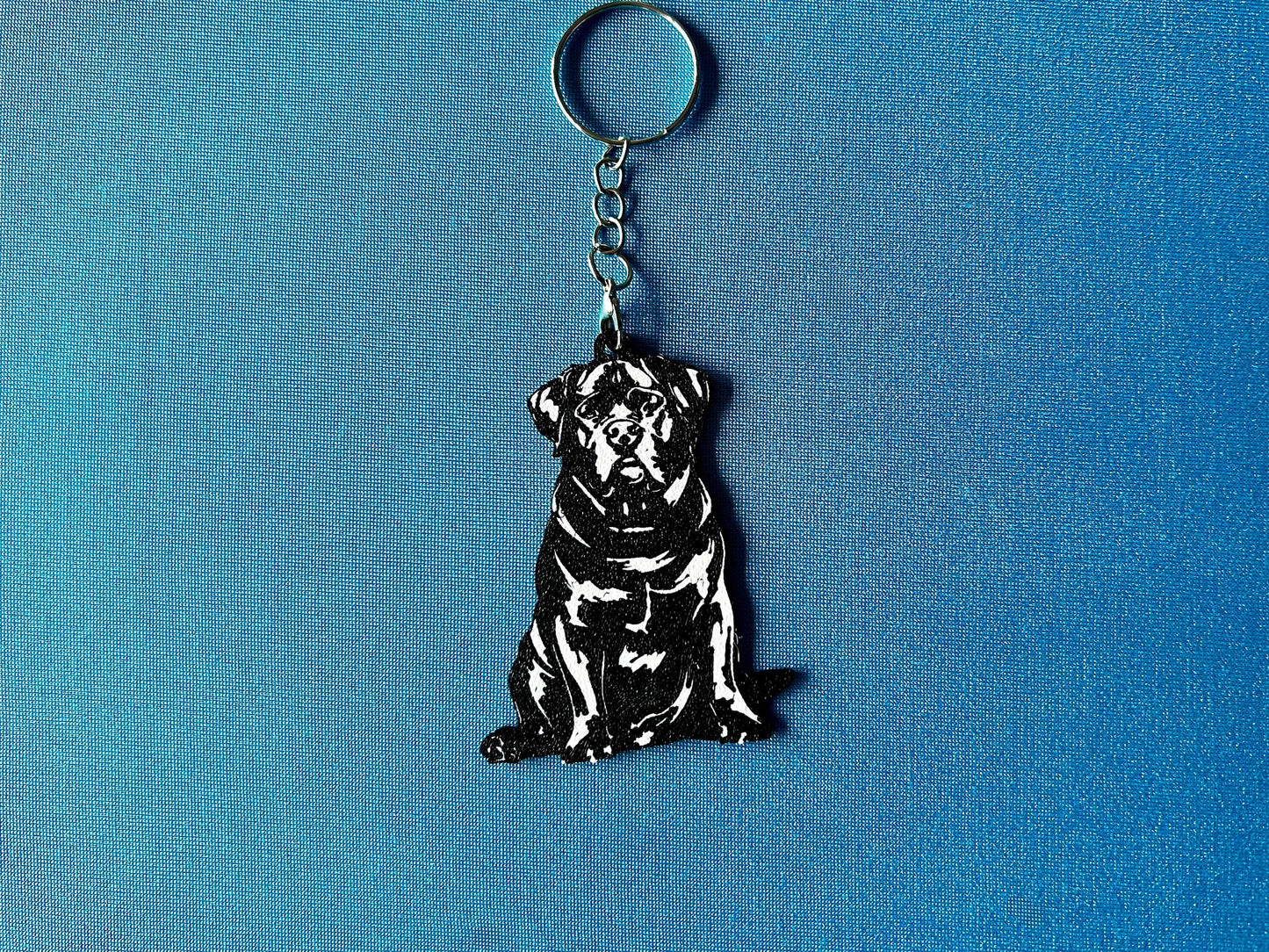 Rottweiler Silhouette Keyring laying on a blue table cloth. The keyring features a white background with a black silhouette of a Rottweiler.