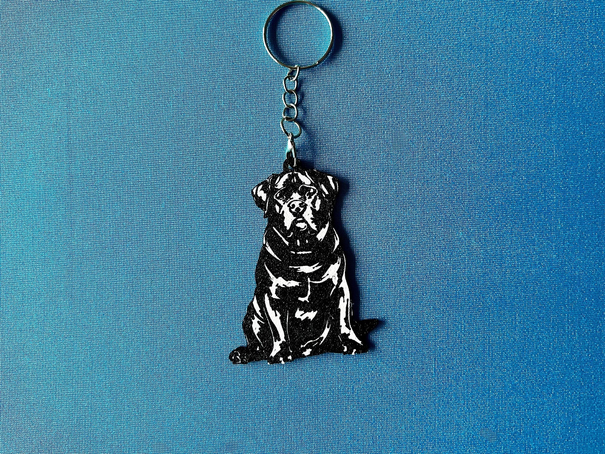 Rottweiler Silhouette Keyring laying on a blue table cloth. The keyring features a white background with a black silhouette of a Rottweiler.