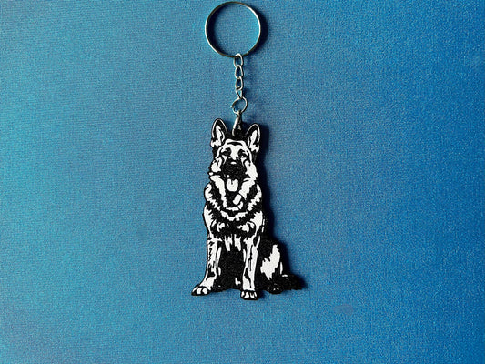 German Shepherd Silhouette Keyring laying on a blue table cloth. The keyring features a white background with a black silhouette of a German Shepherd.