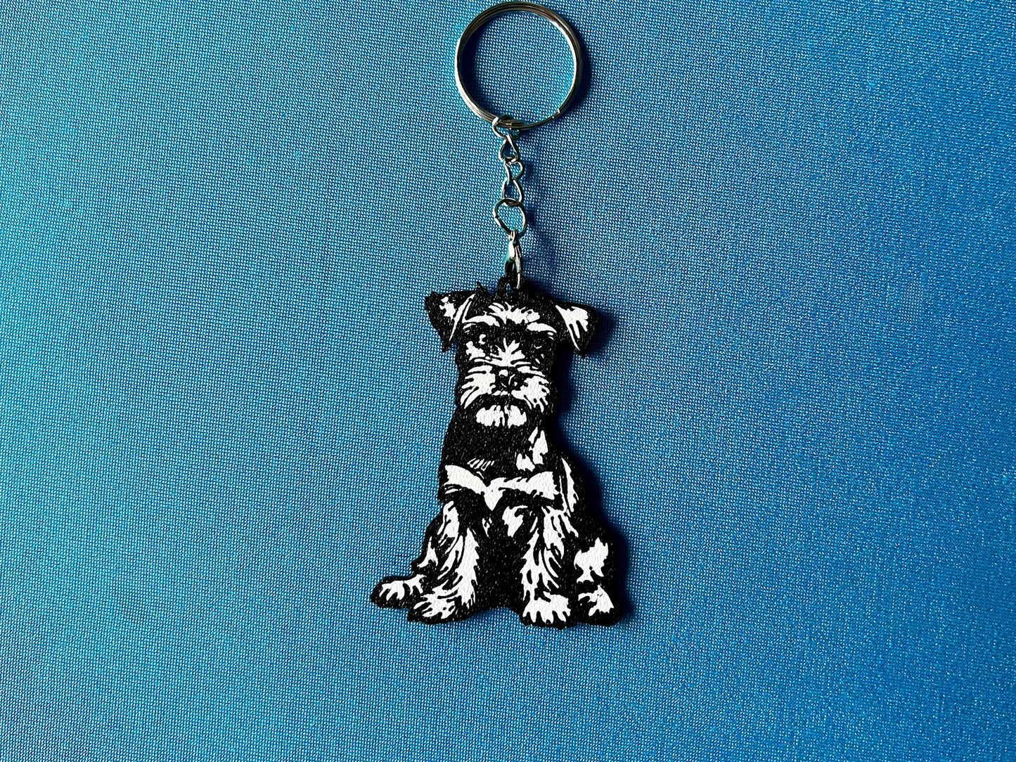 Miniature Schnauzer Silhouette Keyring laying on a blue table cloth. The keyring features a white background with a black silhouette of a Miniature Schnauzer.