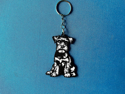 Miniature Schnauzer Silhouette Keyring laying on a blue table cloth. The keyring features a white background with a black silhouette of a Miniature Schnauzer.