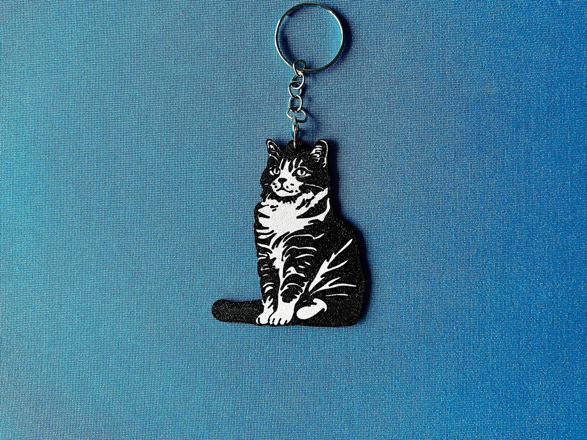 American Bobtail Silhouette Keyring laying on a blue table cloth. The keyring features a white background with a black silhouette of a American Bobtail.