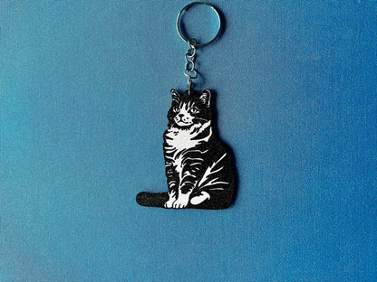 American Bobtail Silhouette Keyring laying on a blue table cloth. The keyring features a white background with a black silhouette of a American Bobtail.