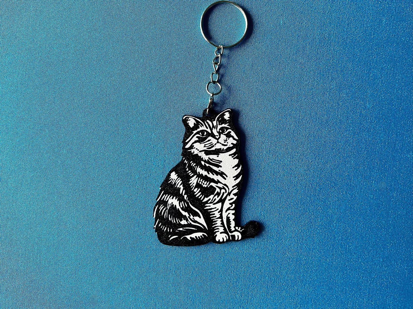 Highland Fold Silhouette Keyring laying on a blue table cloth. The keyring features a white background with a black silhouette of a Highland Fold.