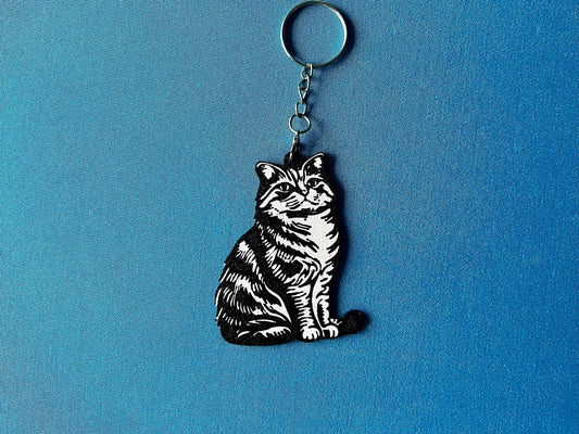 Highland Fold Silhouette Keyring laying on a blue table cloth. The keyring features a white background with a black silhouette of a Highland Fold.