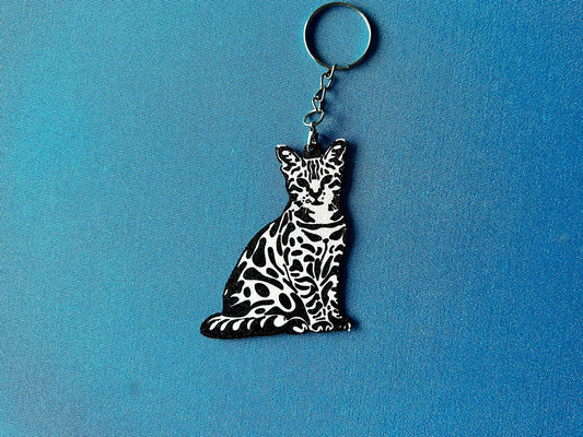 Bengal Silhouette Keyring laying on a blue table cloth. The keyring features a white background with a black silhouette of a Bengal.