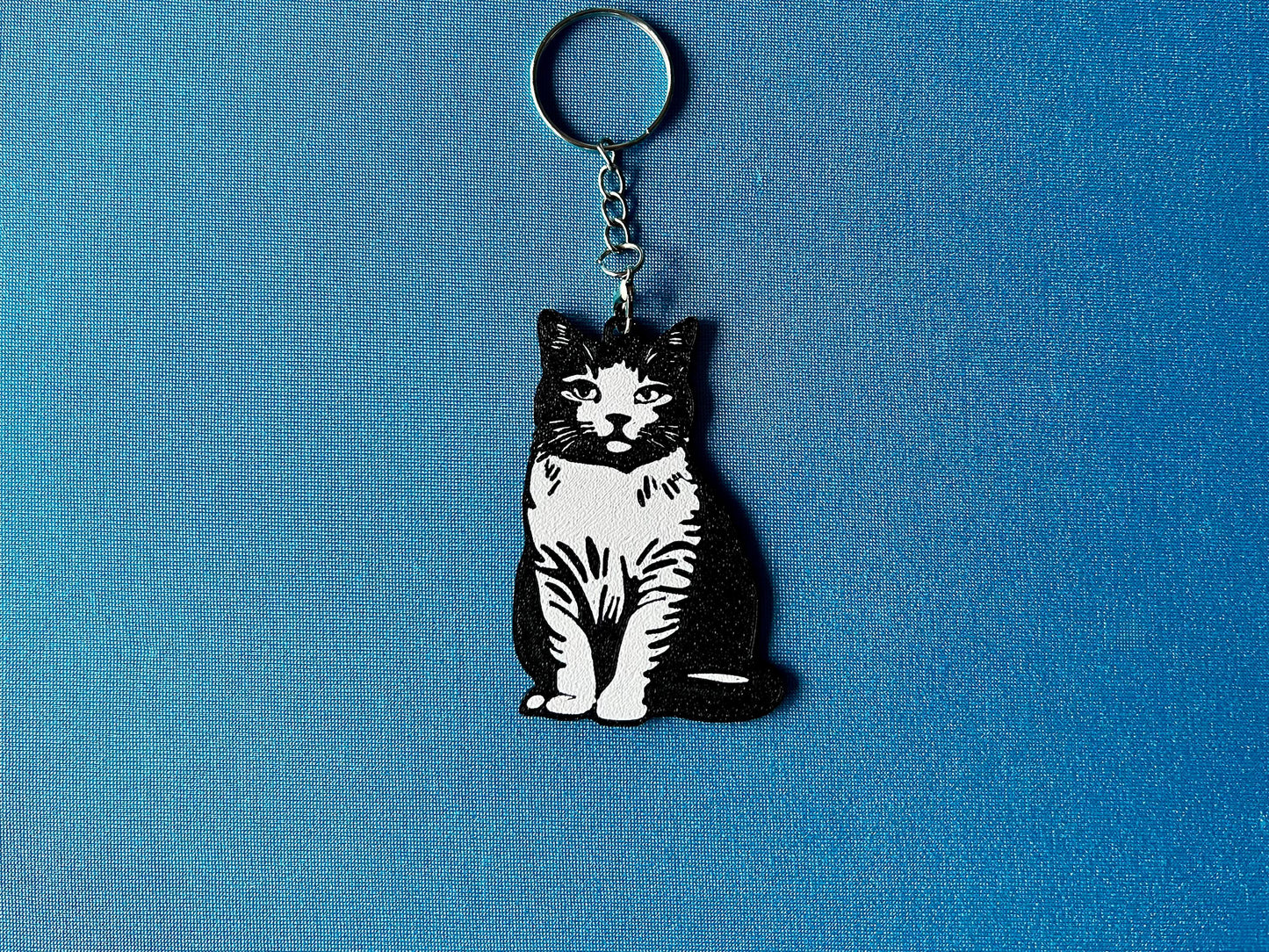British Shorthair Silhouette Keyring laying on a blue table cloth. The keyring features a white background with a black silhouette of a British Shorthair.