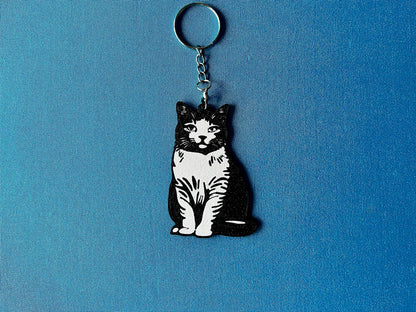 British Shorthair Silhouette Keyring laying on a blue table cloth. The keyring features a white background with a black silhouette of a British Shorthair.