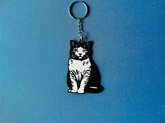 British Shorthair Silhouette Keyring laying on a blue table cloth. The keyring features a white background with a black silhouette of a British Shorthair.
