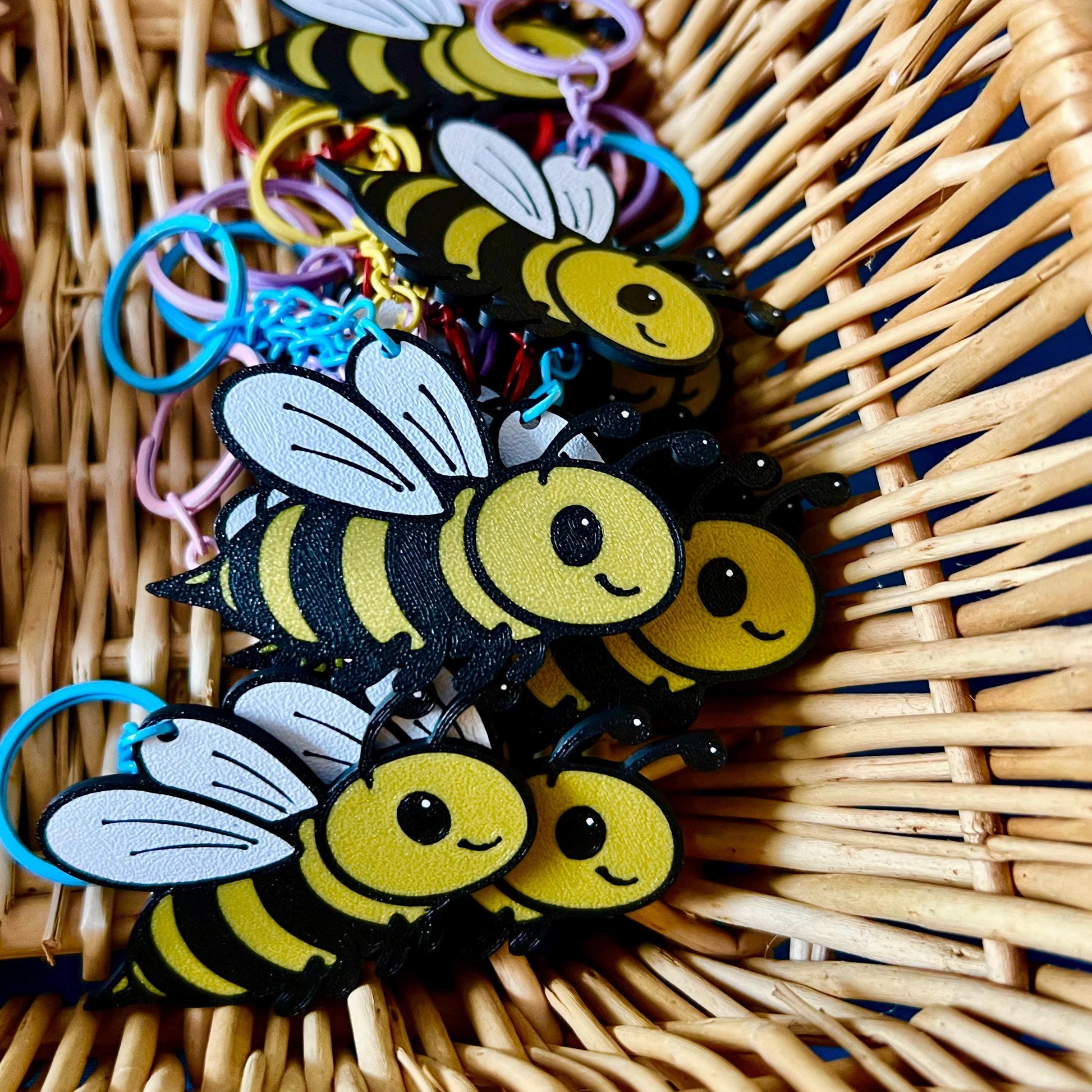 Bee Keyrings, in a basket. The Bee keyrings are made of PLA plastic and are coloured Black, Yellow and White, with a coloured stainless steel key chain.