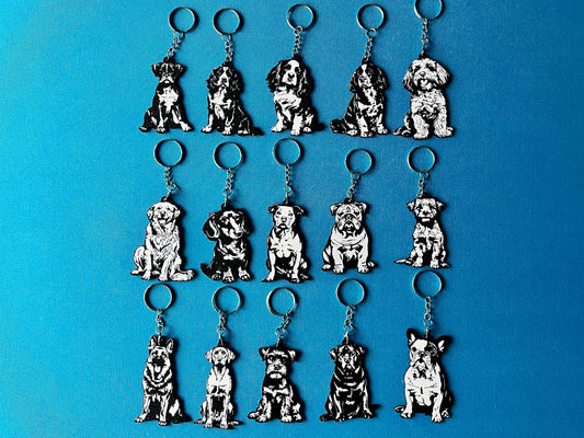 15 Dog breed Silhouette Keyrings laying on a blue table cloth. The keyrings feature a white background with a black silhouette of a dog.
