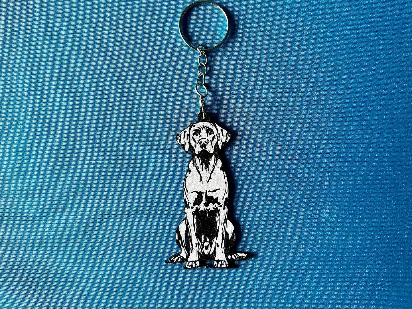 Hungarian Vizsla Silhouette Keyring laying on a blue table cloth. The keyring features a white background with a black silhouette of a Hungarian Vizsla.