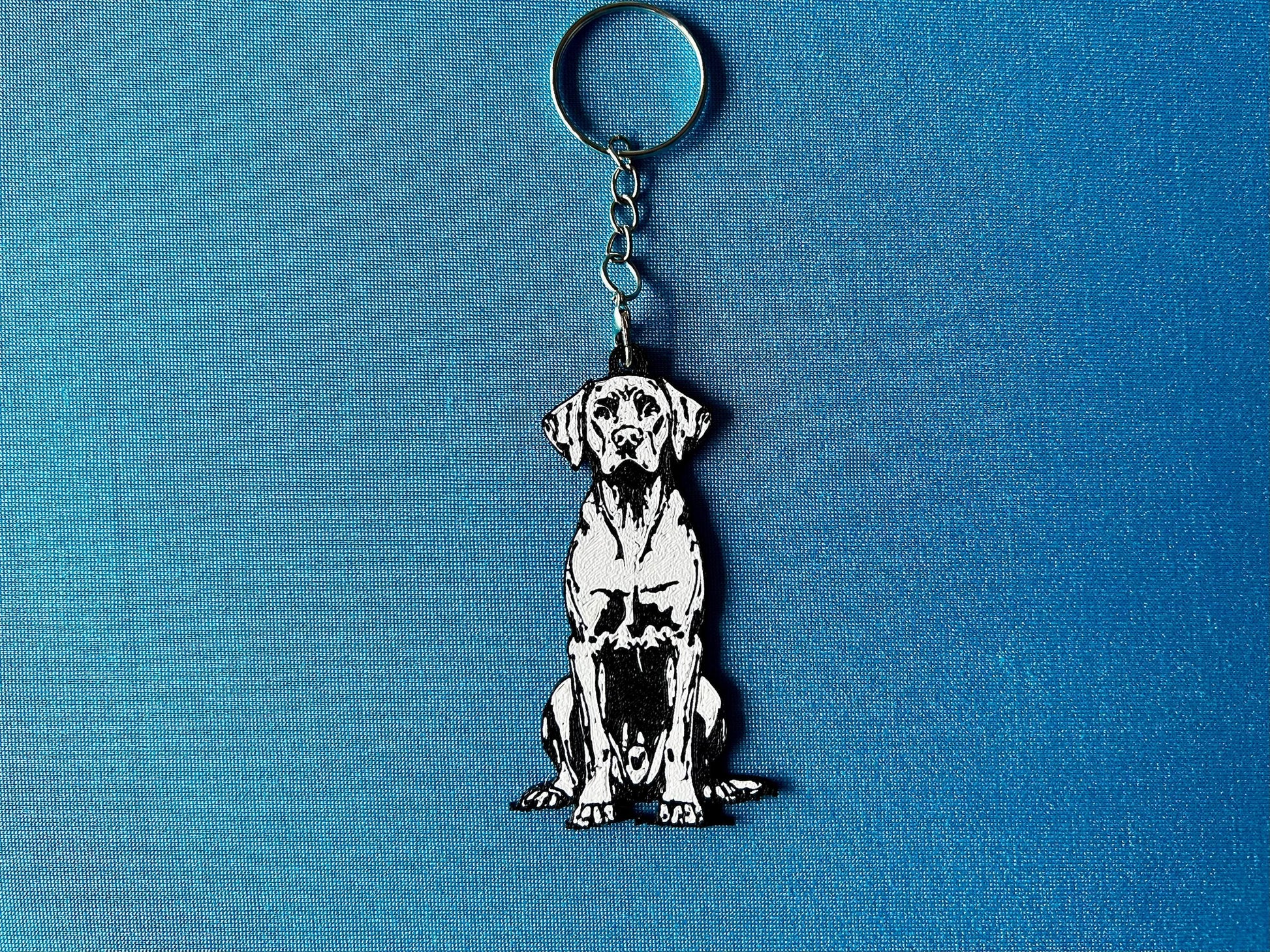 Hungarian Vizsla Silhouette Keyring laying on a blue table cloth. The keyring features a white background with a black silhouette of a Hungarian Vizsla.