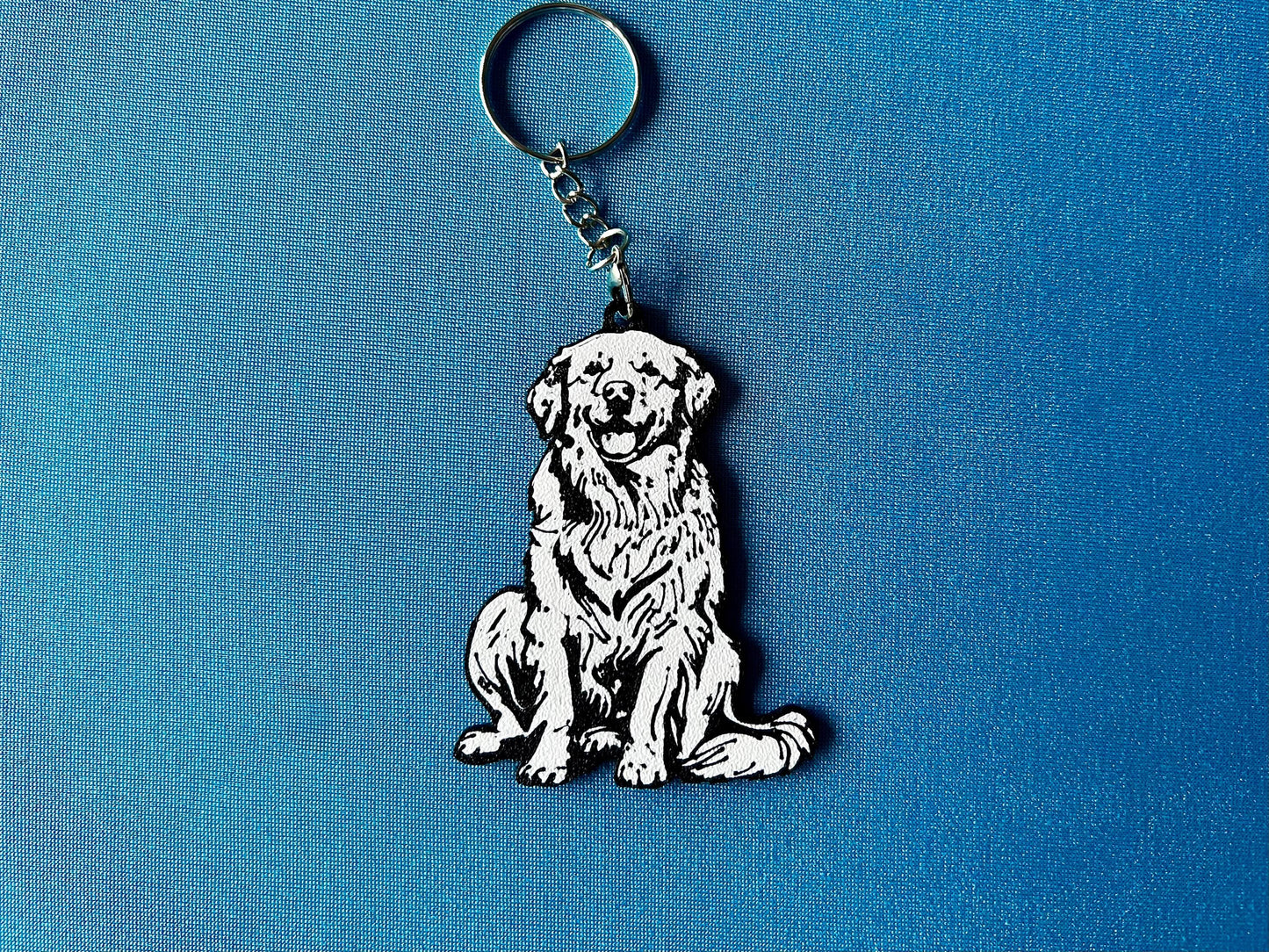 Golden Retriever Silhouette Keyring laying on a blue table cloth. The keyring features a white background with a black silhouette of a Golden Retriever.