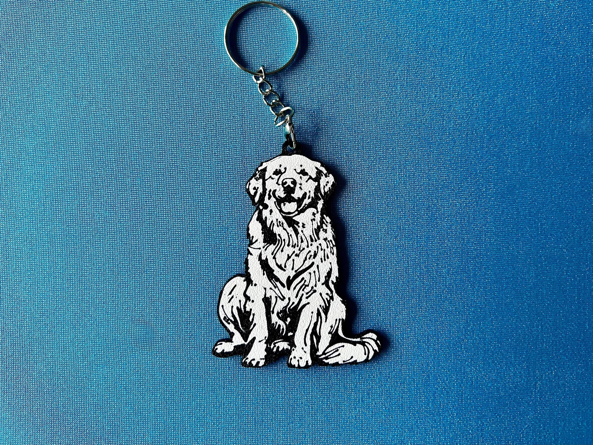 Golden Retriever Silhouette Keyring laying on a blue table cloth. The keyring features a white background with a black silhouette of a Golden Retriever.