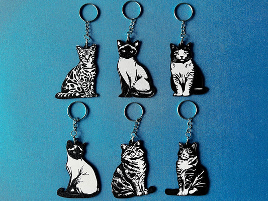 6 Cat breed Silhouette Keyrings laying on a blue table cloth. The keyrings feature a white background with a black silhouette of a cat.