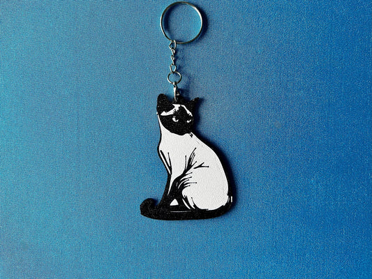 Burmese Silhouette Keyring laying on a blue table cloth. The keyring features a white background with a black silhouette of a Burmese.
